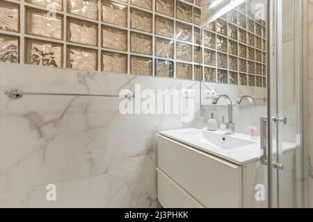 Badezimmer mit Waschbecken aus weißem Harz, Marmorwänden, Glasfenstern und begehbarer Dusche Stockfoto