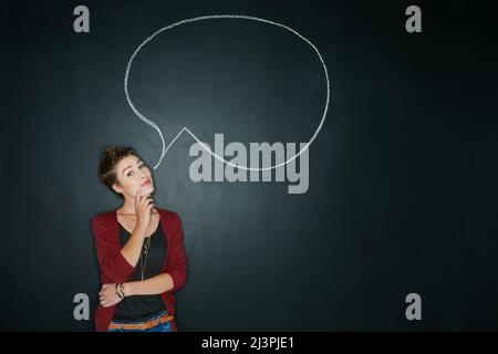 Was ist deine Wahrheit? Studioaufnahme einer jungen Frau, die mit einer Kreidedarstellung einer Sprechblase vor dunklem Hintergrund posiert. Stockfoto