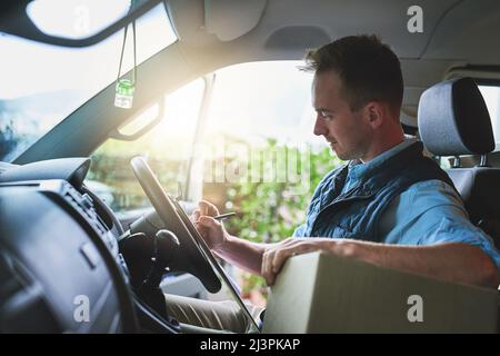 Einhaltung seines Lieferplans. Aufnahme eines Kuriers, der in einem Lieferwagen auf einem Klemmbrett schreibt. Stockfoto