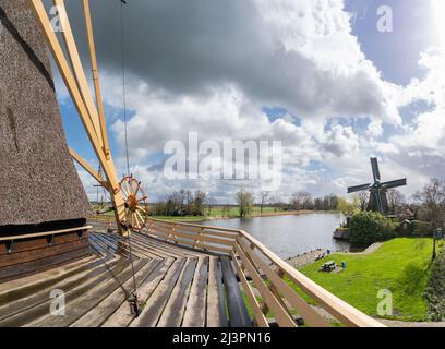 Weesp, Niederlande. 09 april 2022. Bühne, Ankerrad, Tailbeam und Teil der strohgedeckten oberen Struktur der Windmühle 'de Vriendschap' mit Blick auf die Windmühle 'de Eendragt' und den Fluss Vecht. Zusammengeführtem Panorama. Die Gilde der freiwilligen Millers wird 2022 50 Jahre alt. Um die Bedeutung des Müllerhandwerks zu unterstreichen, wurde ein Rekordversuch unternommen, alle niederländischen rotierenden Wind- und Wasserturbinen in den Niederlanden zwischen 11:00 und 12:00 Uhr gleichzeitig laufen zu lassen. Mehr als 800 Mühlen nahmen daran Teil, darunter 29 Mühlen im Ausland. Kredit: Steppeland/Alamy Live Nachrichten Stockfoto