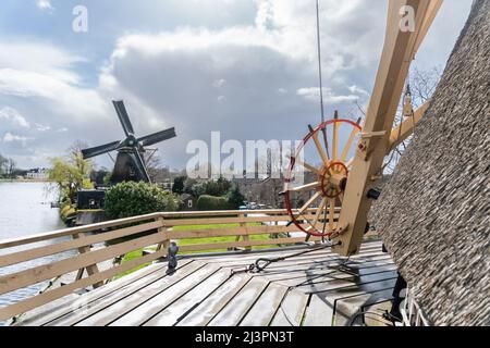 Weesp, Niederlande. 09 april 2022. Bühne, Ankerrad, Tailbeam und Teil der strohgedeckten oberen Struktur der Windmühle 'de Vriendschap' mit Blick auf die Windmühle 'de Eendragt' und den Fluss Vecht. Die Gilde der freiwilligen Millers wird 2022 50 Jahre alt. Um die Bedeutung des Müllerhandwerks zu unterstreichen, wurde ein Rekordversuch unternommen, alle niederländischen rotierenden Wind- und Wasserturbinen in den Niederlanden zwischen 11:00 und 12:00 Uhr gleichzeitig laufen zu lassen. Mehr als 800 Mühlen nahmen daran Teil, darunter 29 Mühlen im Ausland. Kredit: Steppeland/Alamy Live Nachrichten Stockfoto