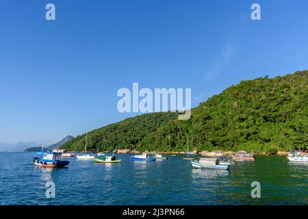 Fischerboote schwimmen auf ruhigen Gewässern in der Ilha Grande Bucht in Angra dos Reis mit dem Regenwald und den Hügeln im Hintergrund Stockfoto