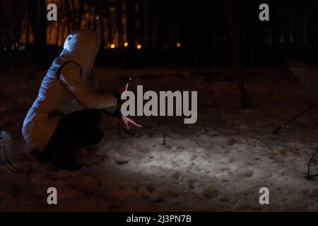 Eine Frau sucht im Winter durch das Licht einer Taschenlampe draußen nach einem verlorenen Ding. Stockfoto