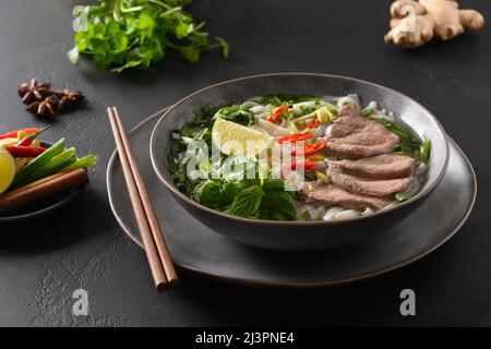 Pho Bo traditionelle Suppe mit Rindfleisch, Reisnudeln, Ingwer, Limette, Chili in einer Schüssel. Nahaufnahme. Vietnamesische und asiatische Küche. Stockfoto