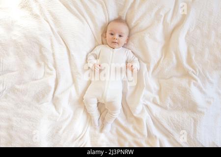 Baby auf einer weißen Decke. Baby liegt auf einer weißen Musselindecke auf dem Boden und schaut auf die Kamera. Stockfoto