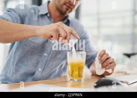 Ich hoffe, dass dies auch meinen Schmerz auflösen wird. Ausgeschnittene Aufnahme eines nicht erkennbaren Geschäftsmannes, der einen Beutel Medizin in einem Glas Wasser in einem auflöst Stockfoto