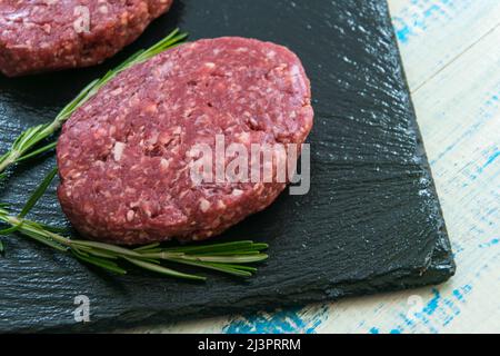 Zwei rohe Hackfleischpasteten auf einer schwarzen Steinoberfläche. Stockfoto