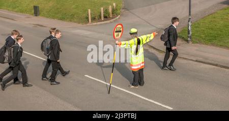 Lollipop Lady und Schüler überqueren die Straße England, Großbritannien Stockfoto