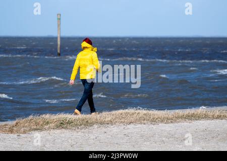 Harlesiel, Deutschland. 09. April 2022. Bei sonnigem Wetter läuft ein Mann am Strand vor der Nordsee entlang. Mit dem Beginn der Ferien in vielen deutschen Bundesländern, darunter Nordrhein-Westfalen, reisten am Samstag viele Osterurlauber an die Küste und die ostfriesischen Inseln. Quelle: Hauke-Christian Dittrich/dpa/Alamy Live News Stockfoto