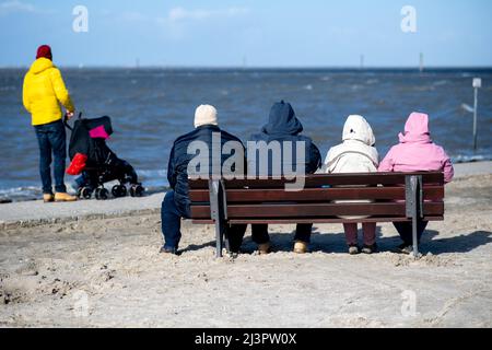 Harlesiel, Deutschland. 09. April 2022. Bei sonnigem Wetter sitzen Touristen auf einer Bank am Strand. Mit dem Beginn der Ferien in vielen deutschen Bundesländern, darunter Nordrhein-Westfalen, reisten am Samstag viele Osterurlauber an die Küste und die ostfriesischen Inseln. Quelle: Hauke-Christian Dittrich/dpa/Alamy Live News Stockfoto