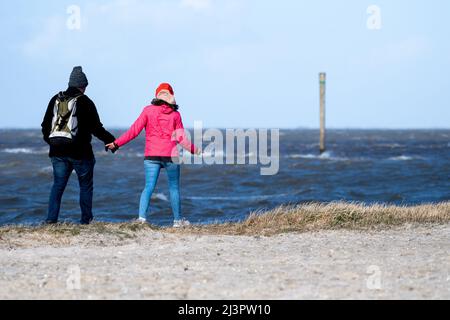 Harlesiel, Deutschland. 09. April 2022. Bei sonnigem Wetter läuft ein Vater mit seiner Tochter am Strand vor der Nordsee entlang. Mit dem Beginn der Ferien in vielen deutschen Bundesländern, darunter Nordrhein-Westfalen, reisten am Samstag viele Osterurlauber an die Küste und die ostfriesischen Inseln. Quelle: Hauke-Christian Dittrich/dpa/Alamy Live News Stockfoto