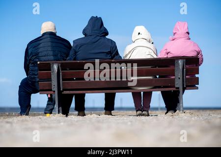 Harlesiel, Deutschland. 09. April 2022. Bei sonnigem Wetter sitzen Touristen auf einer Bank am Strand. Mit dem Beginn der Ferien in vielen deutschen Bundesländern, darunter Nordrhein-Westfalen, reisten am Samstag viele Osterurlauber an die Küste und die ostfriesischen Inseln. Quelle: Hauke-Christian Dittrich/dpa/Alamy Live News Stockfoto