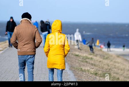 Harlesiel, Deutschland. 09. April 2022. Bei sonnigem Wetter laufen Touristen am Hafen entlang eines Deiches. Mit dem Beginn der Ferien in vielen deutschen Bundesländern, darunter Nordrhein-Westfalen, reisten am Samstag viele Osterurlauber an die Küste und die ostfriesischen Inseln. Quelle: Hauke-Christian Dittrich/dpa/Alamy Live News Stockfoto