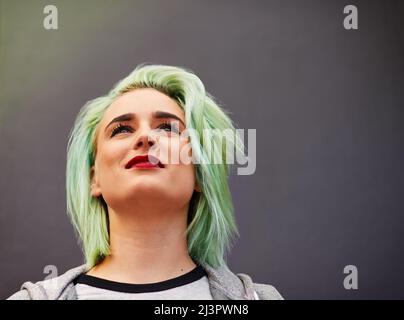 Auf der Oberseite der neuesten Haar-Trends. Aufnahme einer trendigen jungen Frau mit mintgrünen Haaren, die vor einem grauen Hintergrund posiert. Stockfoto