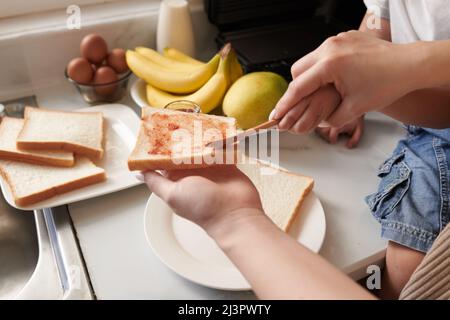 Hände der Mutter lehren kleinen Sohn Speading Marmelade auf Sandwich-Brot Stockfoto