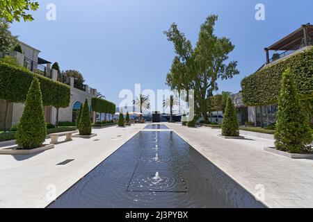 TIVAT, MONTENEGRO - 15. JULI 2021: Luxuriöse Promenade mit Brunnen auf dem Bürgersteig und geformten Bäumen in Porto Montenegro Stockfoto