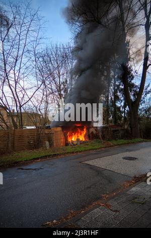 Der Gartenschuppen hat Feuer gefangen und brennt mit lodernden Flammen und dunklen Rauchwolken nieder Stockfoto