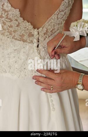 Nahaufnahme der Hände beim letzten Knöpfen des Brautkleides Stockfoto