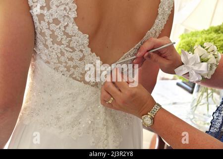 Nahaufnahme der Hände beim letzten Knöpfen des Brautkleides Stockfoto