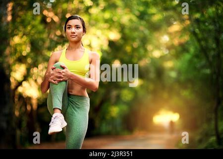 Machen Sie sich bereit, die Straße zu gehen. Aufnahme einer jungen Frau, die sich vor ihrem Lauf dehnt. Stockfoto