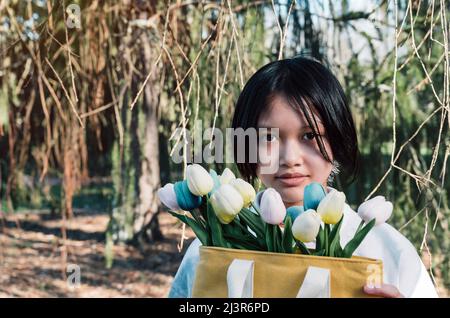 Portrait von Teenager-Asian Mädchen hält Strauß von Tulpen Blumen in der Tasche. Copy space. Stockfoto