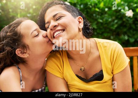 Küsse für Mama. Eine kurze Aufnahme eines entzückenden kleinen Mädchens, das ihre Mutter auf die Wange küsst, während sie im Park ist. Stockfoto