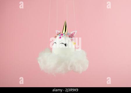 Ostereinhorn-Ei fliegt auf Wolke auf pastellrosa Hintergrund. Frohe ostern Banner. Inspiration für Aktivitäten für Kinder. Grußkarte oder Poster. Speicherplatz kopieren für Stockfoto