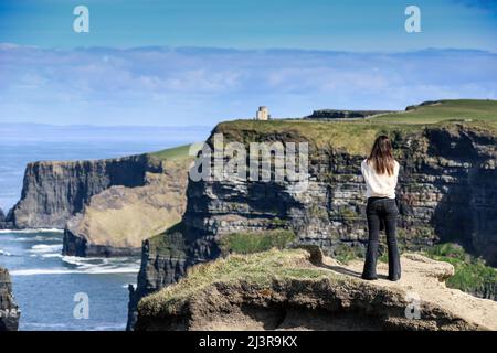 Eine Frau bewundert die Cliffs of Moher Views, Meeresklippen am südwestlichen Rand der Region Burren in der Grafschaft Clare, Irland Stockfoto