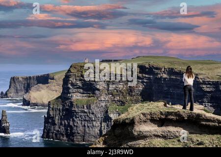 Eine Frau bewundert die Cliffs of Moher Views, Meeresklippen am südwestlichen Rand der Region Burren in der Grafschaft Clare, Irland Stockfoto