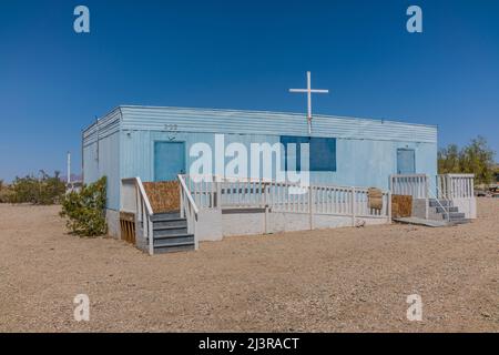 Eine blaue Anhängerkirche in Slab City, Kalifornien, mit einem weißen Holzkreuz oben und mit Treppen an beiden Enden. Die Kirche ist über eine lange ADA zugänglich Stockfoto