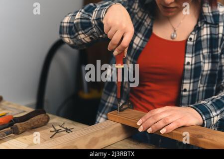 Nahaufnahme der Hände eines jungen rothaarigen Zimmermanns mit einem Schraubendreher auf einem Holzbrett. Stockfoto