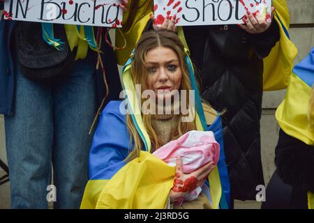 London, Großbritannien. 9.. April 2022. Ein Protestler hält ein symbolisches „Baby“, das mit gefälschtem Blut bedeckt ist. Demonstranten inszenierten einen massiven "Einmarsch" und hielten Schilder mit gefälschtem Blut bedeckt, um gegen das Massaker in der Stadt Bucha und die Gräueltaten zu protestieren, die angeblich von russischen Truppen in der Ukraine begangen wurden. Kredit: Vuk Valcic/Alamy Live Nachrichten Stockfoto