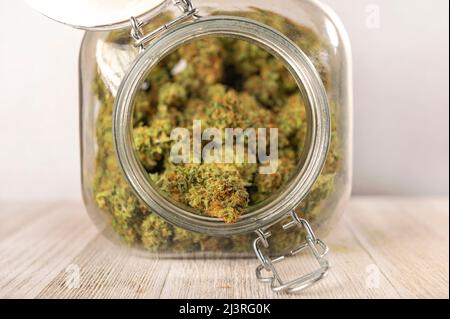 Getrocknete Cannabisknospen, die in einem Glasgefäß auf weißem Hintergrund isoliert aufbewahrt werden Stockfoto