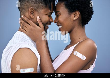 Wir entschieden uns, zusammen zu leben und wurden geimpft. Aufnahme eines jungen Paares, das sich im Studio umarmte, nachdem es seine Covid-Impfstoffe erhalten hatte. Stockfoto