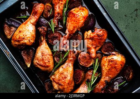 Gebackene Hähnchenbeine, Drumsticks mit süßen Feigen und Zwiebeln in balsamischer Marinade auf schwarzem Backblech, rostiger grüner Tischhintergrund, Draufsicht Stockfoto