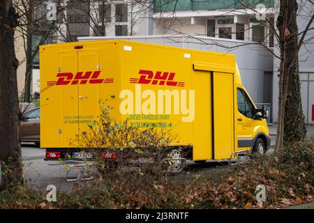 Gelbe DHL-Parkplätze vor Gebäuden. Baum und Sträucher stehen im Vordergrund. Zustellung von Paketen und Paketen an Kunden zu Hause. Stockfoto