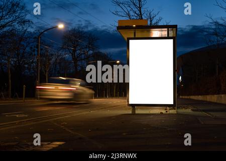 Leere Werbetafel als Mock-up-Vorlage in der Stadt. Leerer Bildschirm an einer Bushaltestelle in der Nacht. Ein Autofahrer kommt sehr schnell vorbei. Stockfoto