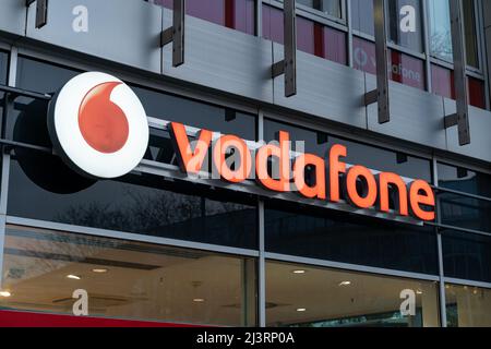 Vodafone Shop in der Stadt. Beleuchtetes Logo und Schriftzug an der Fassade eines Gebäudes. Eines der großen Telekommunikationsunternehmen in Deutschland. Stockfoto