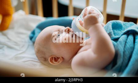 Baby Kleinkind liegt auf der blauen Decke, trinkt Milch aus der Flasche. Titelbild Stockfoto