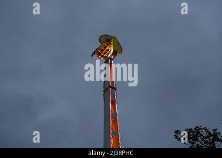 Fairground Ride sehr hoch in der Luft vor einem dunklen Himmel. Bunte Lichter der Maschine leuchten hell. Schwingender Arm auf dem Jahrmarkt. Stockfoto