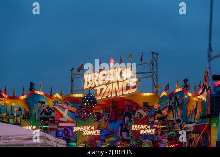 Breakdance Funfair Ride mit einem großen beleuchteten Logo am Abend. Die Fahrt auf dem Messegelände dreht sich sehr schnell. Freizeitaktivitäten in Deutschland. Stockfoto