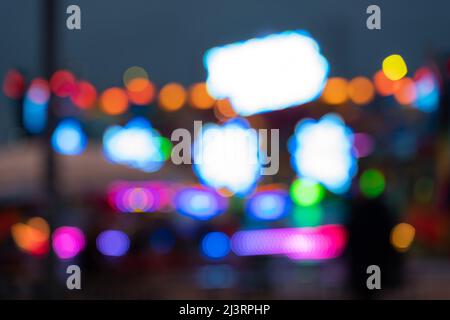 Verschwommener Hintergrund des Messegeländes mit vielen leuchtenden Lichtern. Verschwommenes Vergnügungspark mit nicht identifizierbaren Menschen wegen Bokeh. Defokussierte abstrakte Szene. Stockfoto