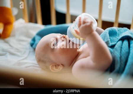 Baby Kleinkind liegt auf der blauen Decke, trinkt Milch aus der Flasche. Stockfoto