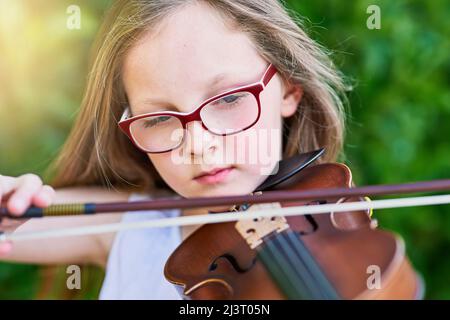 Shes bekam natürlich geborene musikalische Begabung. Ein kleiner Schuss eines Mädchens, das draußen Geige spielt. Stockfoto