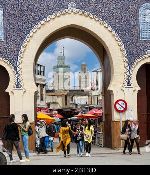 Fes, Marokko.  Junge Frauen in modernen marokkanischen Kleid verlassen Fes El-Bali (Altstadt) durch die Bab Boujeloud.  Das Minarett der Medersa Bou Inania ich Stockfoto