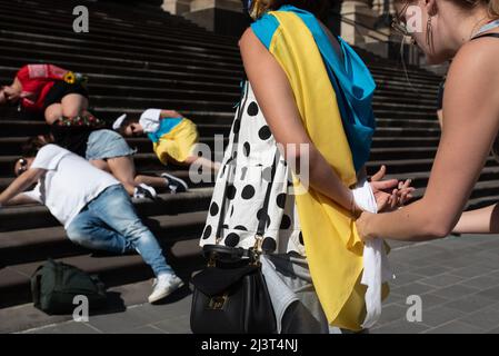 Melbourne, Australien. 10. April 2022. Eine Frau wird mit weißem Tuch in die Hände gebunden, während andere auf den Stufen des Parlamentshauses in Melbourne liegen, als Teil einer Demonstration als Reaktion auf russische Soldaten, die ukrainische Zivilisten töten. Quelle: Jay Kogler/Alamy Live News Stockfoto