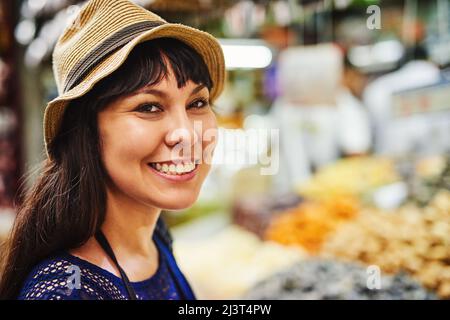 So viel zu sehen, so viel zur Auswahl. Porträt einer fröhlichen jungen Frau, die tagsüber mitten auf einem geschäftigen Markt draußen steht. Stockfoto