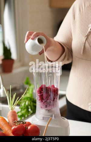 Plus-Size-Frau gießt nicht-MilchNerz in den Mixer mit geschnittenen roten Drachenfrüchten Stockfoto