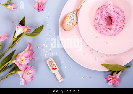 Draufsicht flach Lay Frühling oder Sommer Komposition in pastellrosa und blauen Farben von Tellern, Donut und Blumen. Selektiver Fokus. Stockfoto