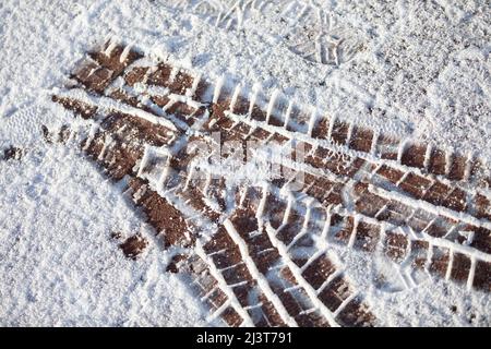 Frische Reifenspuren auf weichem Schnee auf einem Bürgersteig in der Stadt. Stockfoto